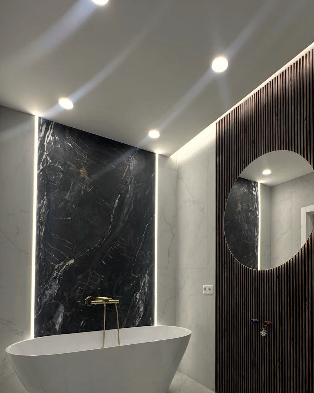 Bagno con vasca freestanding, lastra effetto marmo nero e rubinetteria oro